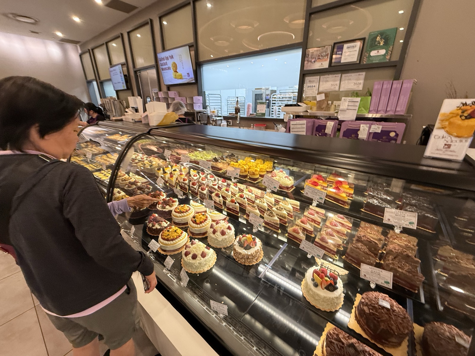 A customer choosing cakes at the display case beneath framed certificates
