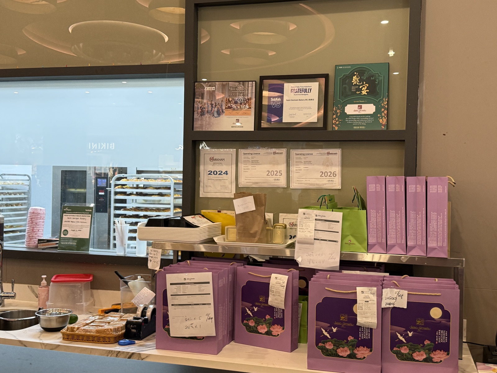 Three sponsor recognition pieces displayed on a shelf above Markham operating licences at Saint Germain Bakery